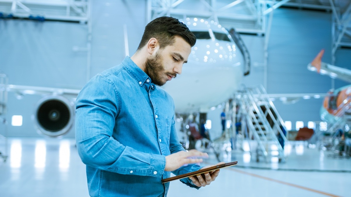 a technician in an airport hangar reviewing work instructions examples on their tablet